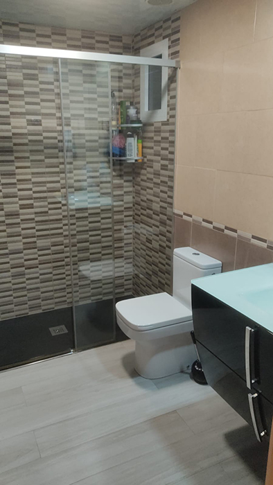 lavabo amb dutxa negra amb mampara i diferents tipus de rajoles a la zona d'aigües